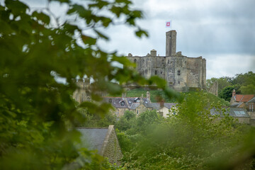 View of medieval Warkworth Castle from afar with tree and foliage in the way for artistic effect