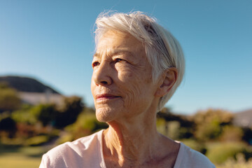 Close-up of serious asian senior woman contemplating against clear blue sky in yard, copy space