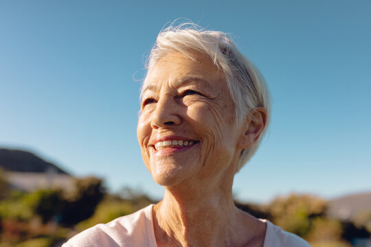 Close-up of cheerful asian senior woman with short hair looking away against clear blue sky in yard