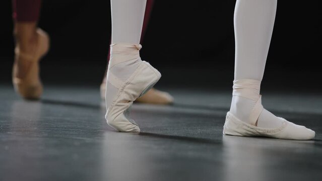 Unrecognizable student ballerina repeats movements after teacher spin foot. Two pairs of female legs on floor do ballet twist exercises stand on pointe shoes couple ballerinas dance together in class
