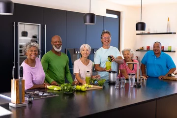 Tuinposter Portrait of cheerful multiracial senior friends preparing smoothie in kitchen at retirement home © wavebreak3