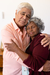 Multiracial senior couple with eyes closed embracing against white wall in retirement home