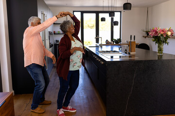 Full length of romantic multiracial senior couple dancing in kitchen at retirement home, copy space