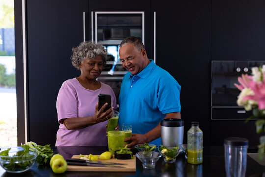 African american senior woman showing mobile phone to caucasian man in kitchen at retirement home - Powered by Adobe