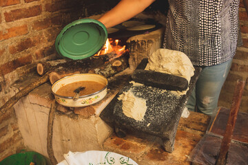 Mujer mexicana torteando maza de maíz en un metate y una estufa de leña para hacer tortillas...