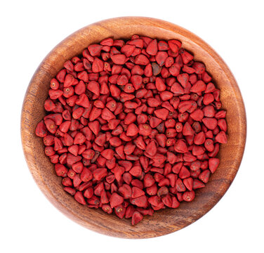 Annatto seeds in wooden bowl, isolated on a white background. Achiote seeds, bixa orellana. Natural dye for cooking and food. Close-up. Top view.
