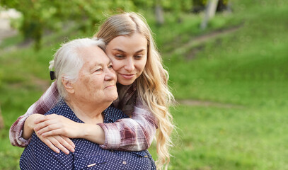 Happy adult granddaughter hugging old grandmother outdoors in summer