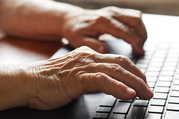 Close-up of the hand of an old retired person using a laptop