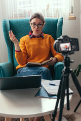 Woman coach or psychologist conducts online conference and records video on camera for blog at home