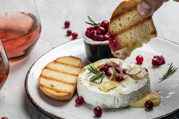 Baked camembert cheese with cranberries, basil leaves and rosemary on light table. French cuisine. Food recipe background. Close up