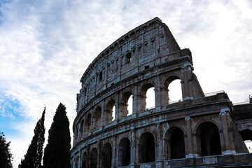 Panoramic view on exterior facade of famous Colosseum (Coloseo) of city of Rome, Lazio, Italy, Europe. UNESCO World Heritage Site. Flavian Amphitheater of ancient Roman Empire. Tree in foreground