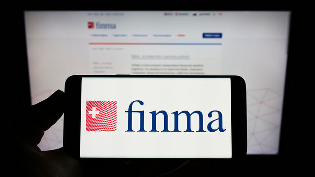 Stuttgart, Germany - 06-04-2022: Person holding cellphone with logo of Eidgenoessische Finanzmarktaufsicht (FINMA) on screen in front of webpage. Focus on phone display.