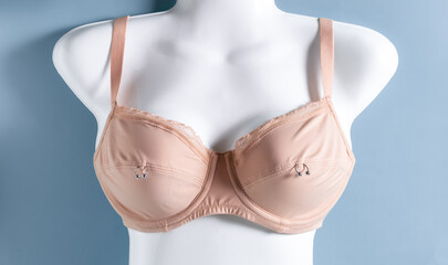 Beige bra on white mannequin with metal rings. Nipple piercing concept.