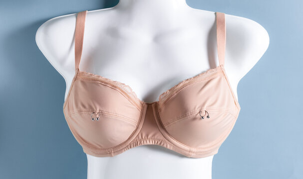 Beige bra on white mannequin with metal rings. Nipple piercing concept.