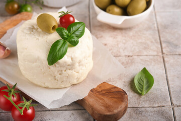 Ricotta cheese. Homemade Ricotta cheese with basil, garlic, tomatoes and green olives on parchment paperback and stand on old beige tiles background. Italian food.  Selective focus.