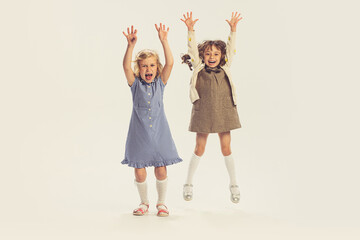 Portrait of two cheerful little girls, children jumping, playing isolated over grey studio background