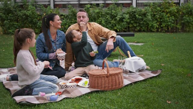 Happy young family sitting on blanket and having take away picnic outdoors in restaurant area. - Powered by Adobe