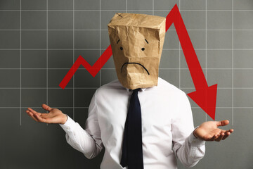 Man wearing paper bag with drawn sad face and illustration of falling down chart on light grey...