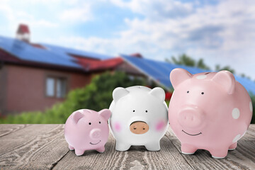 Piggy banks on wooden surface and blurred view of beautiful house. Mortgage concept
