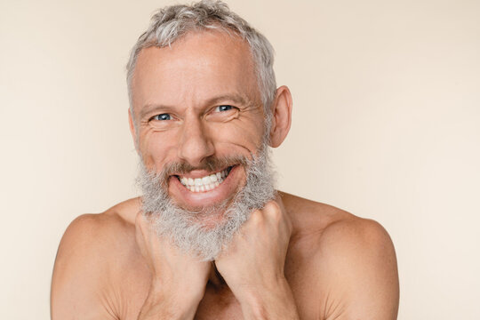 Closeup cropped image of smiling with toothy smile caucasian middle-aged mature man shirtless with grey hair beard isolated in beige background. Male body beauty care