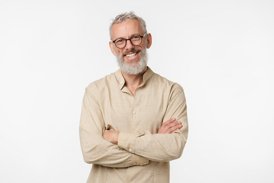Smart caucasian mature middle-aged freelancer man in beige shirt wearing glasses looking at camera with arms crossed isolated in white background