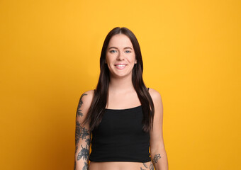 Obraz premium Beautiful woman with tattoos on arms against yellow background