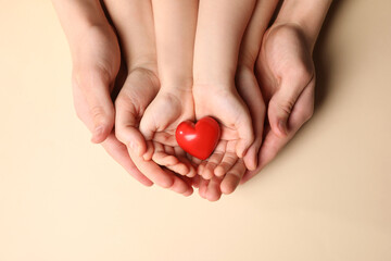Parents and kid holding red heart in hands on beige background, top view