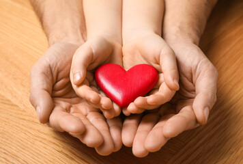 Man and kid holding red heart in hands at wooden table, closeup