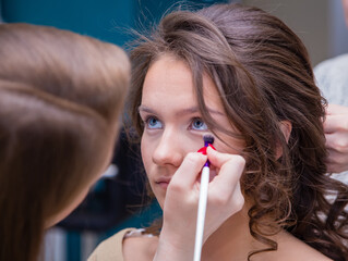 Make-up artist with a brush close-up paints the eyelid of a girl in the salon. Female master makes makeup to a young woman. Business concept - beauty salon, facial skin care, cosmetology.