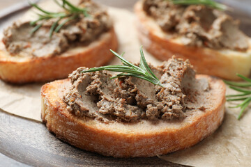 Slices of bread with delicious pate and rosemary on wooden board, closeup