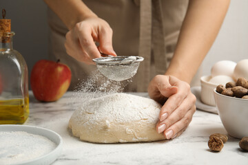 Fototapeta premium Woman sprinkling flour onto dough at white marble table, closeup
