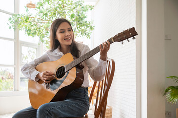 Asian woman enjoys playing guitar at home, hobby and relax leisure concept.