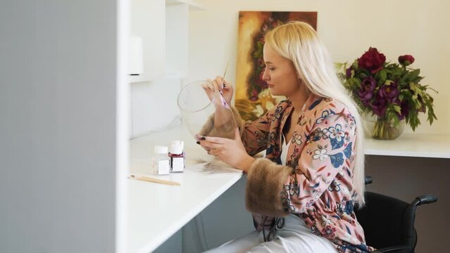 Young female painter painter on glassware sitting in wheelchair