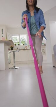 Vertical video of happy biracial woman moping floor