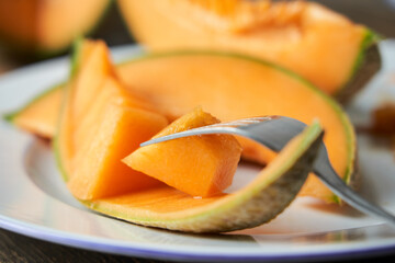 Fototapeta na wymiar Close-up Slices of Japanese melons, honey melon or cantaloupe. taking a piece of melon with a fork. Best fruit in summer. Fruit. Healthy food concept. Front-view