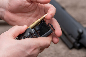 A male hunter loads cartridges for a rifle magazine, equip a combat weapon.