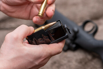 A male hunter loads cartridges for a rifle magazine, equip a combat weapon.