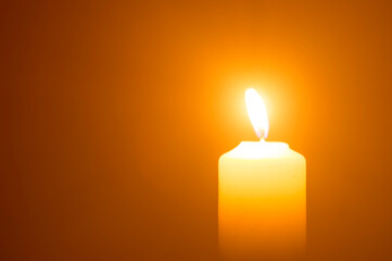 Blurred photo of single burning candle flame or light glowing on a yellow candle on orange or red...