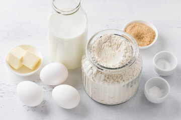 Ingredients for homemade pancakes: milk, flour, eggs, butter, sugar, salt, baking powder on a light blue background, top view. Cooking delicious homemade food