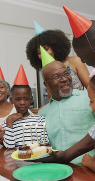 Vertical video of happy african american grandfather celebrating birthday with family at home