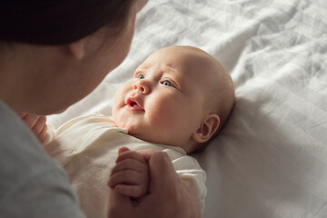 Cute little baby girl enjoys parent attention lying on bed with white sheets. Happy baby face with...