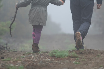 Selective focus shot of back feet of mother and daughter with stick walking in field in foggy...