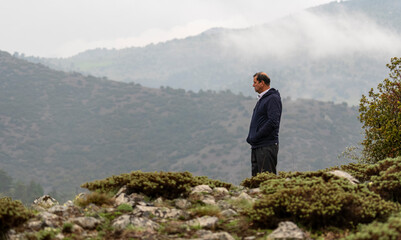 Selective focus shot of depressed old man standing on scree and looking at the foggy landscape.