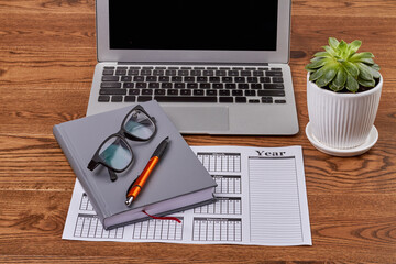 Top view business calendar with laptop and glasses on wooden desk. Office workplace with laptop.