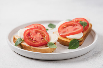 Bruschetta with mozzarella, tomatoes and basil on plate, close-up view