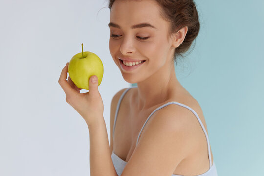 Woman with green apple. Caucasian female model with fresh healthy skin and wavy brown hair looking at green apple that holding in hand. Organic food for healthy eating. 
