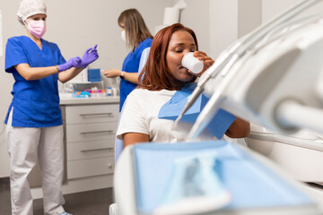 A black woman patient rinses her mouth as a preparation for the dental treatment she is going to receive at the dental clinic