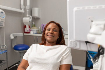 A black woman patient, sit in the dental chair, smiles before having a dental cleaning at the dental center