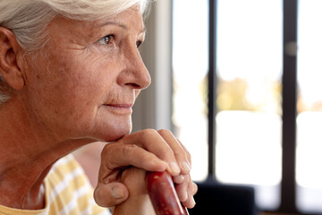 Caucasian senior woman holding a walking stick smiling sitting on the couch at home