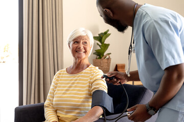 Obraz premium African american male health worker checking blood pressure of caucasian senior woman at home